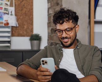 Male with curly hair and glasses smiling at his phone