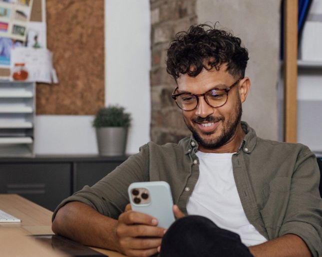 Male with curly hair and glasses smiling at his phone