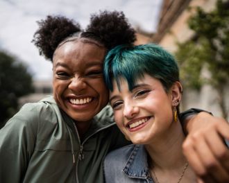 Two females smiling at the camera - one has her arm around the other
