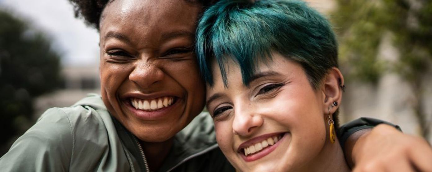 Two females smiling at the camera - one has her arm around the other