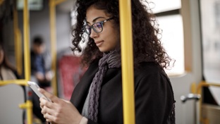 A professional woman in glasses standing on a train looking at her phone