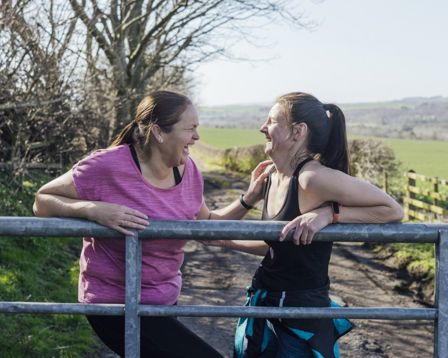 Two women leaning on a metal fence laughing together