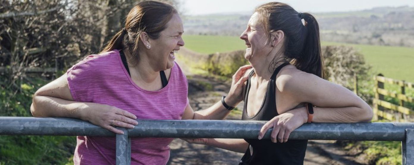 Two women leaning on a metal fence laughing together