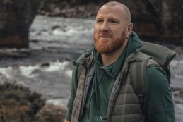 Man looking into the distance with a water and bridge behind in the background