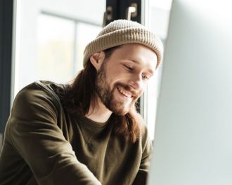 man wearing a hat smiling working on a laptop