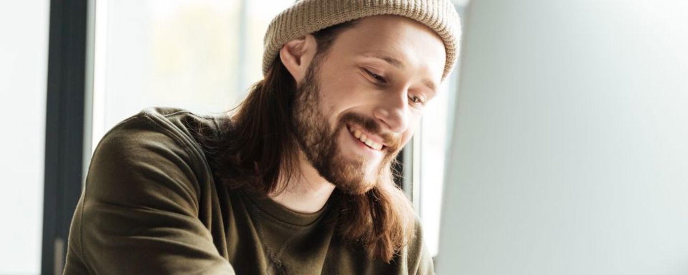 man wearing a hat smiling working on a laptop