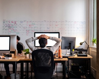 View from behind of a woman sitting at an office desk with her hands on her head