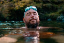 Man with eyes closed with goggles on his head swimming in nature