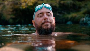 Man with eyes closed with goggles on his head swimming in nature