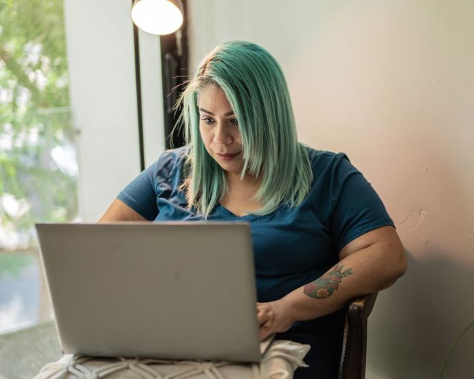 Lady with green hair and tattoos working on her laptop at a table